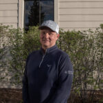 Image of Mark Weinriech standing in front of a building with bushes in the background.